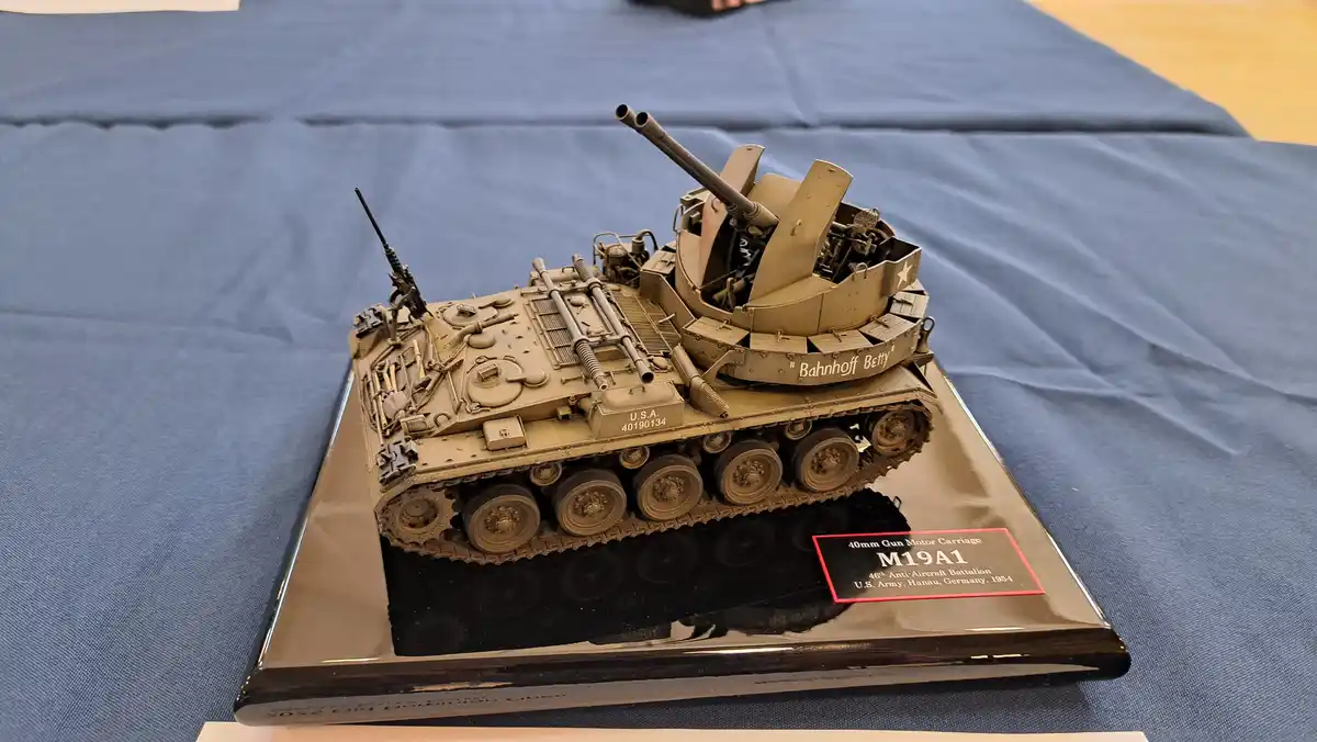 A detailed scale model of a U.S. Army M19A1 40mm Gun Motor Carriage, displayed on a black plaque with a red-bordered label…