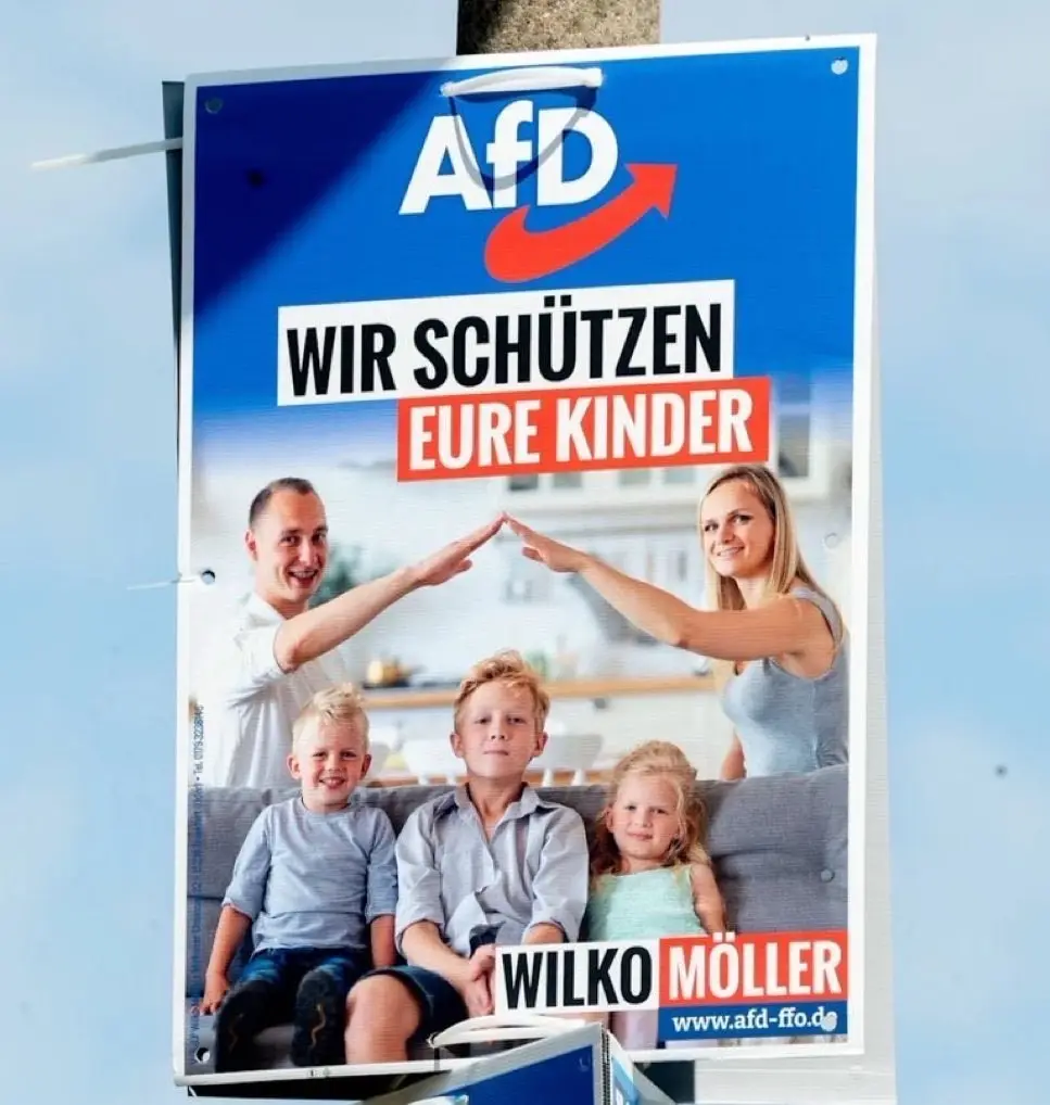 A political campaign poster for the AfD party featuring a smiling family of five with parents forming a protective roof…