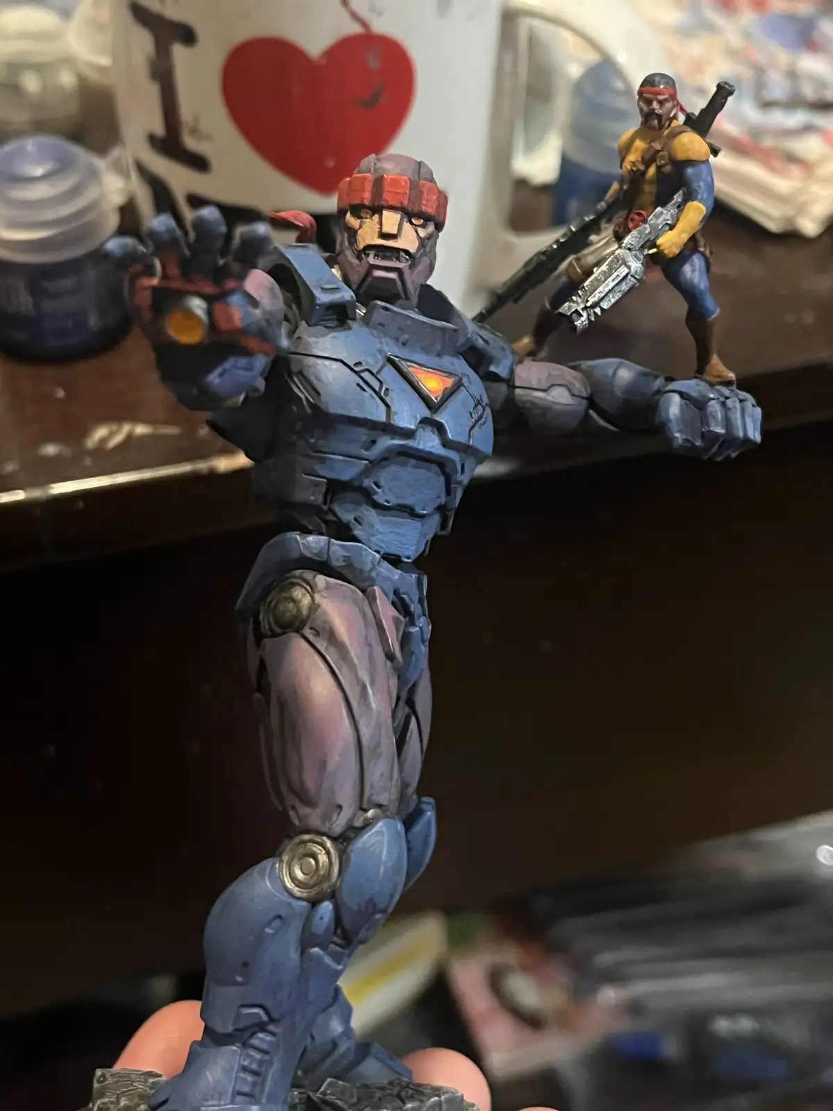 A close-up photo shows a heavily customized, blue-painted action figure of a muscular, armored character with a red headband…