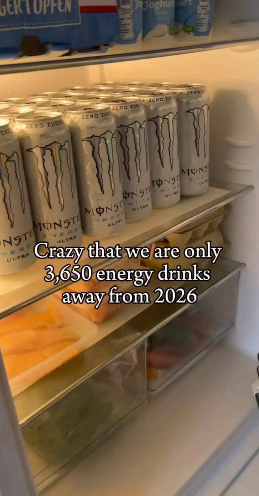 A refrigerator shelf is filled with numerous silver cans of Monster Energy Ultra Zero Sugar. Overlaid text reads: 'Crazy…