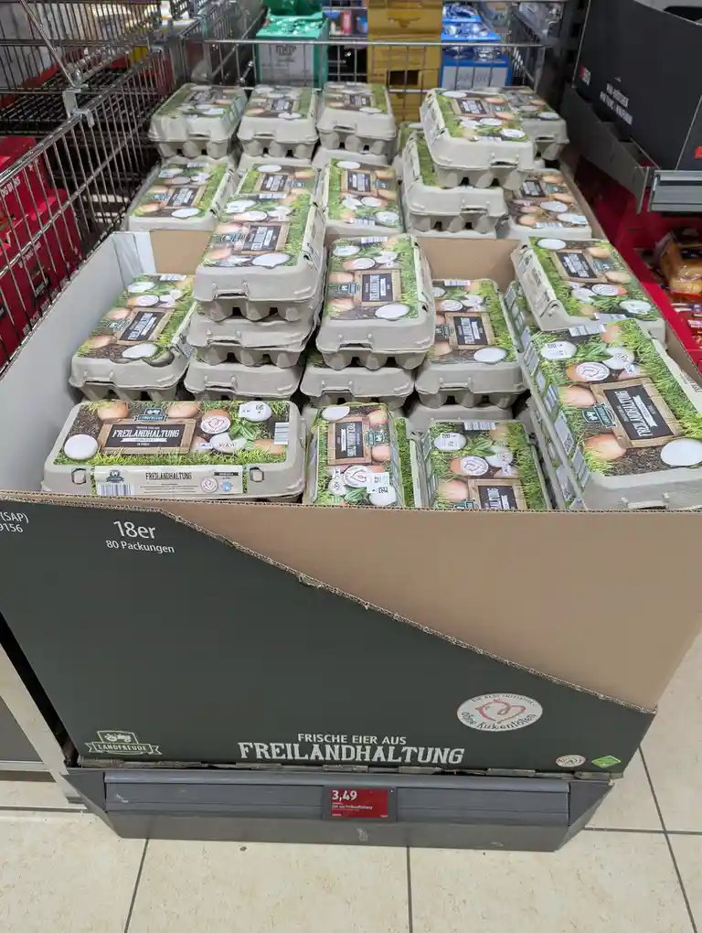 A supermarket display of cardboard egg cartons labeled 'Freilandhaltung' (free-range) are stacked in a large cardboard bin…