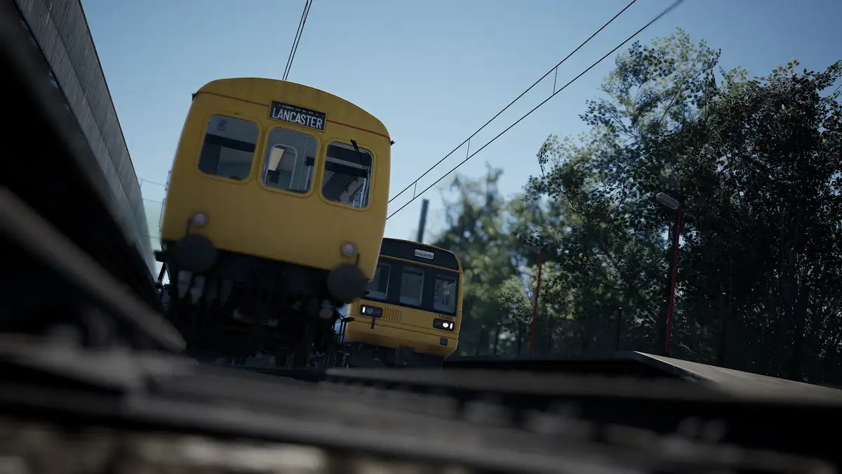 A low-angle shot shows two yellow British trains on parallel tracks, one labeled 'LANCASTER' and the other 'Morecambe'…