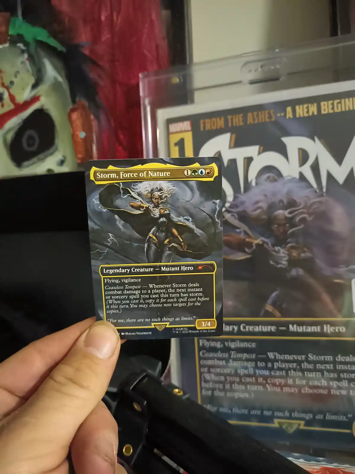 A hand holds a Magic: The Gathering card featuring Storm, Force of Nature, a legendary mutant hero with flying and…