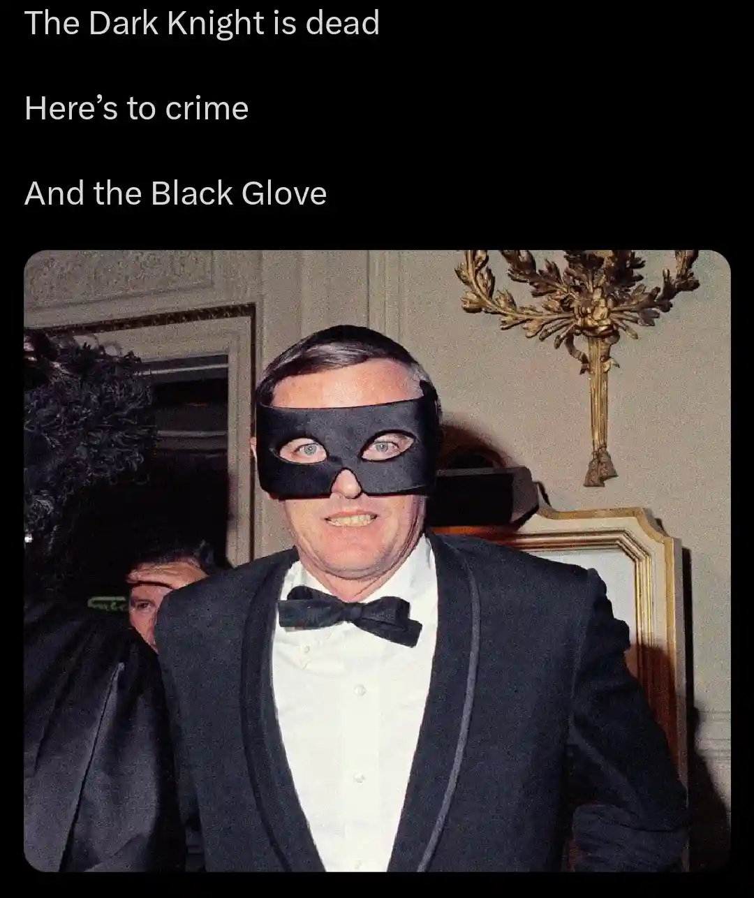 A man in a tuxedo and bowtie wears a black eye mask resembling Batman's, with text above reading 'The Dark Knight is dead'…