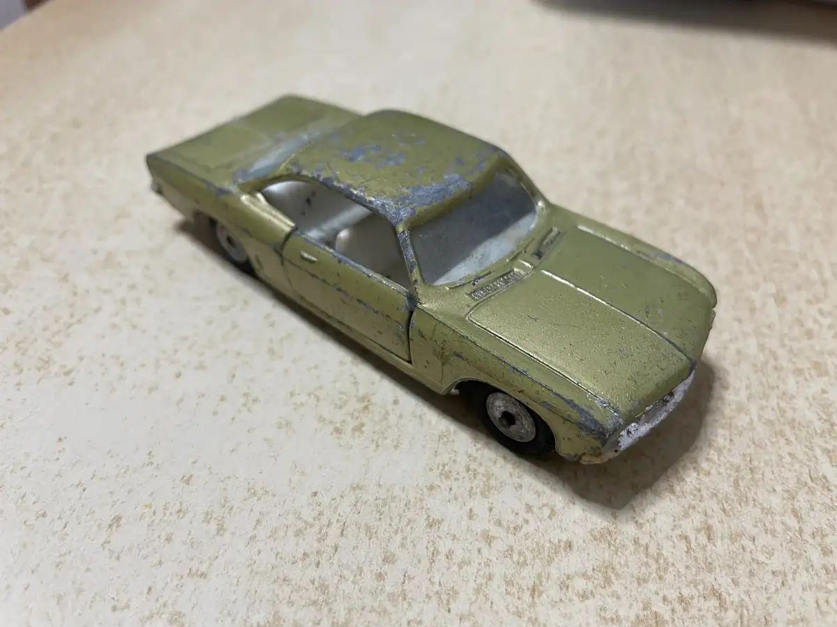 A weathered, olive-green vintage toy car with chipped paint and visible wear sits on a speckled beige countertop. The…