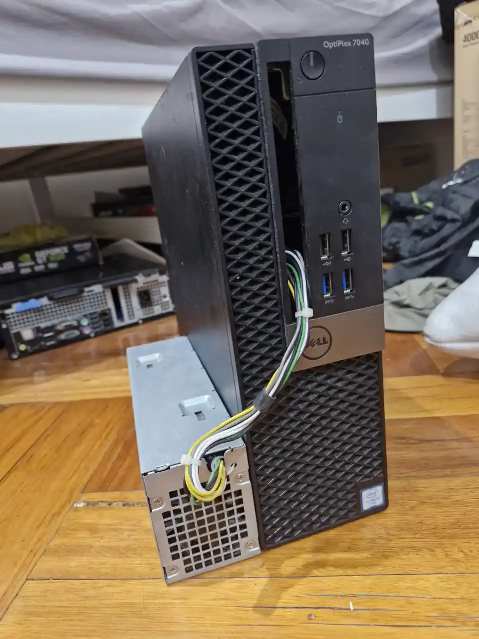 A black Dell OptiPlex 7040 desktop tower sits upright on a wooden floor, with its side panel removed and a separate silver…