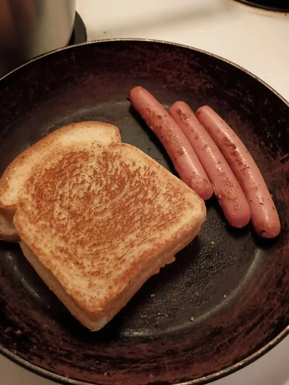 A close-up photo shows a black frying pan on a stovetop containing a single slice of golden-brown toast and three pink…