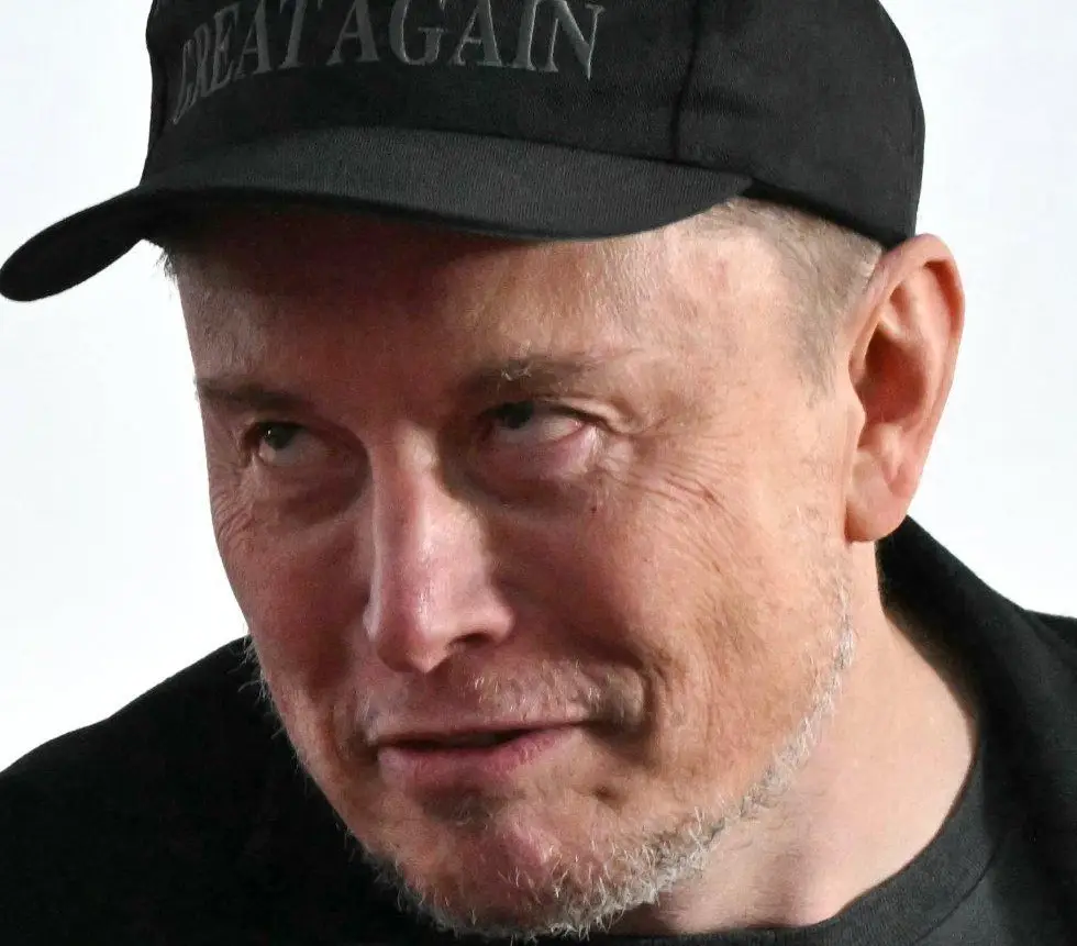 a close-up photo of elon musk wearing a black baseball cap with the words 'GREAT AGAIN' embroidered in gray on the front…