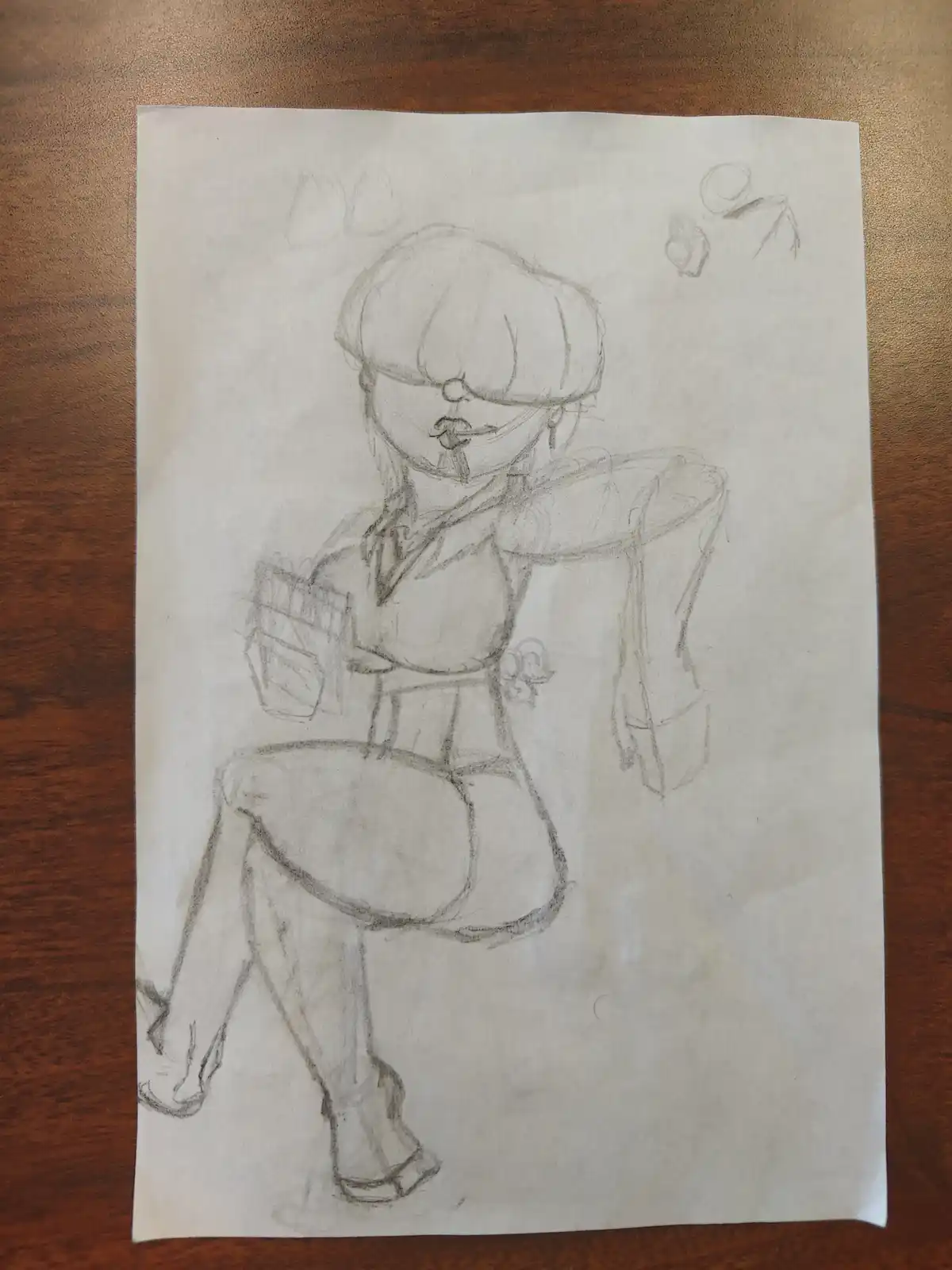 A rough pencil sketch on paper shows a stylized anime-style girl with short hair, sitting and holding a book or tablet. She…