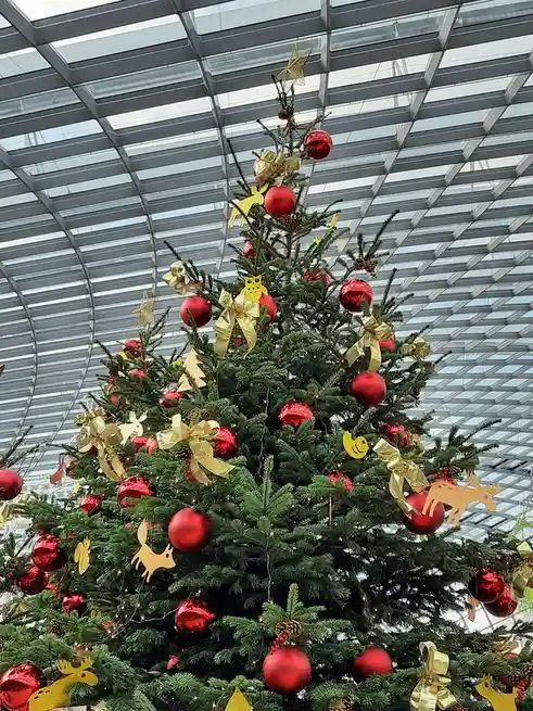 A large, decorated Christmas tree with red ornaments, gold bows, and paper cutouts of animals like reindeer and foxes stands…