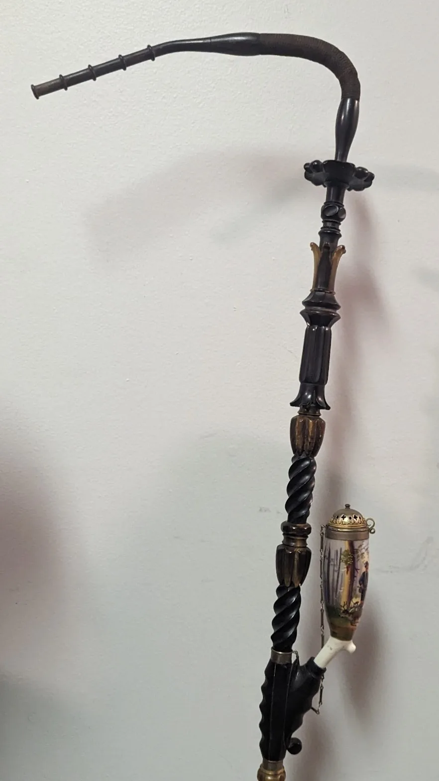 a tall, ornate hookah with a curved black hose, decorative wooden and brass fittings, and a ceramic bowl with painted…