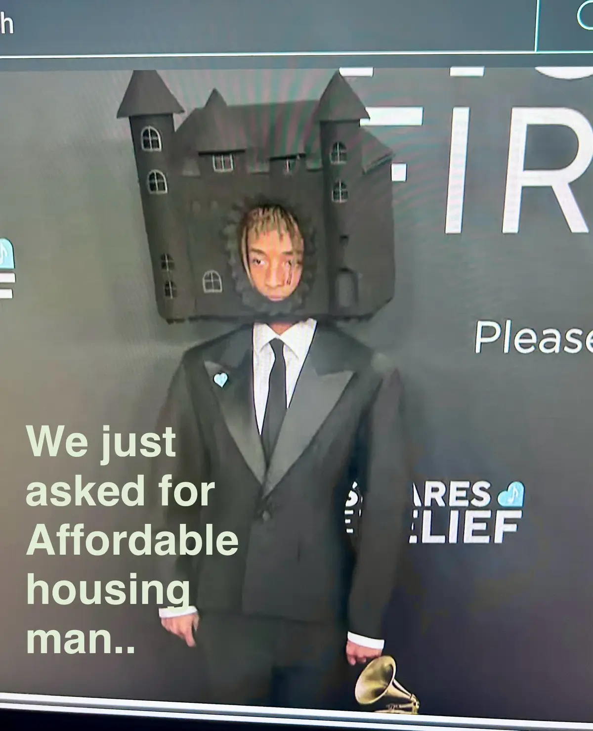 A man in a formal black suit and tie stands with a small golden trophy, his head replaced by a cardboard cutout of a large…