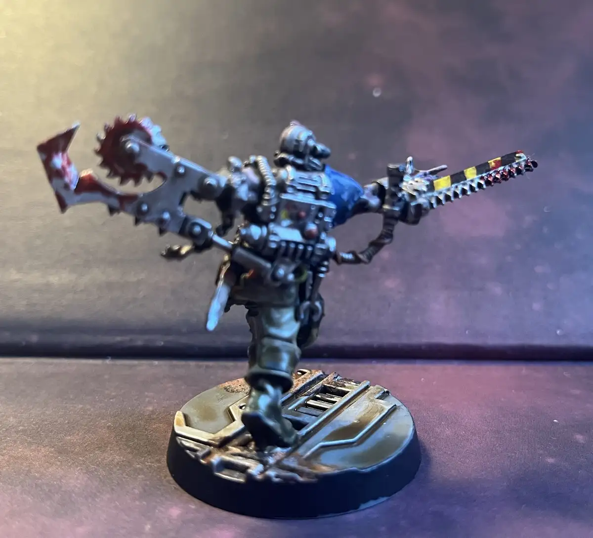 A heavily armored, custom-painted miniature warrior stands on a circular base, wielding two large, ornate, and blood-stained…
