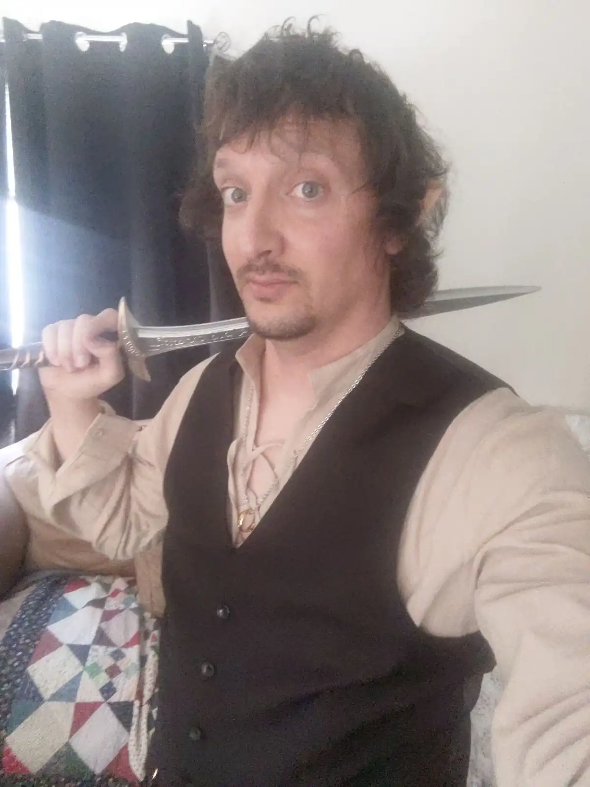 A man with curly hair and pointed ears, dressed in fantasy-themed clothing including a vest and laced shirt, holds a sword…
