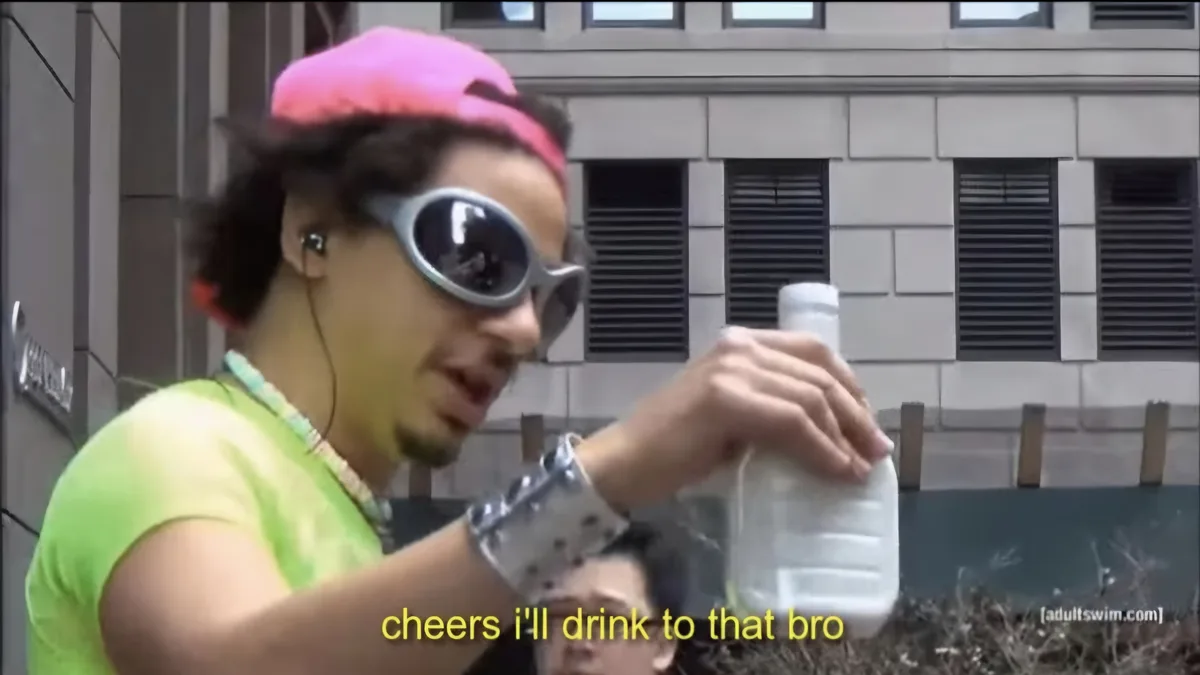 A man wearing a bright pink cap, oversized silver-rimmed sunglasses, and a neon green shirt holds a plastic water bottle…
