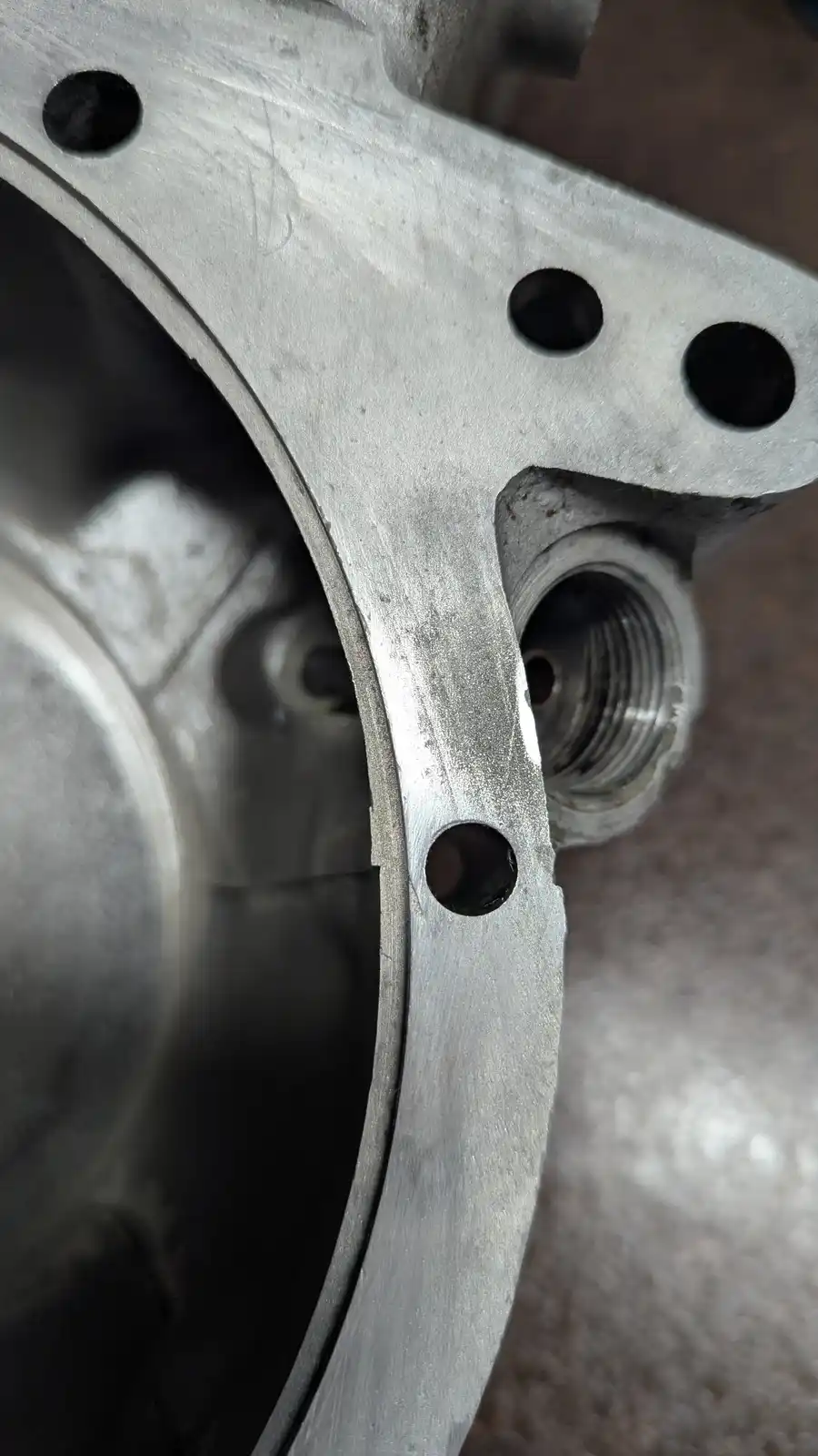 A close-up photo shows a metallic engine component with a smooth, perfectly round hole adjacent to a rough, jaggedly cut…