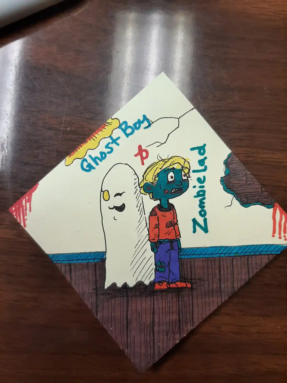 A hand-drawn cartoon on a diamond-shaped paper shows a smiling white ghost labeled 'Ghost Boy' and a blue-skinned zombie boy…