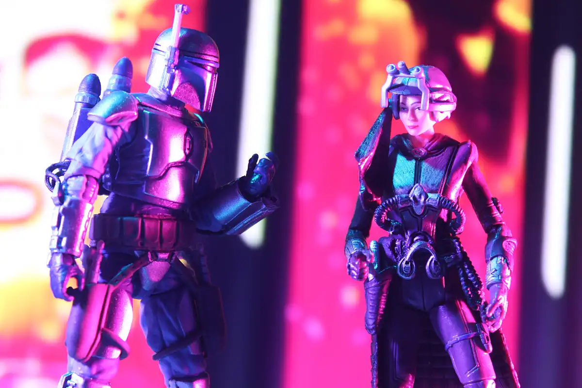 Two Star Wars action figures, one resembling a Mandalorian and the other a female character with a headpiece, stand facing…