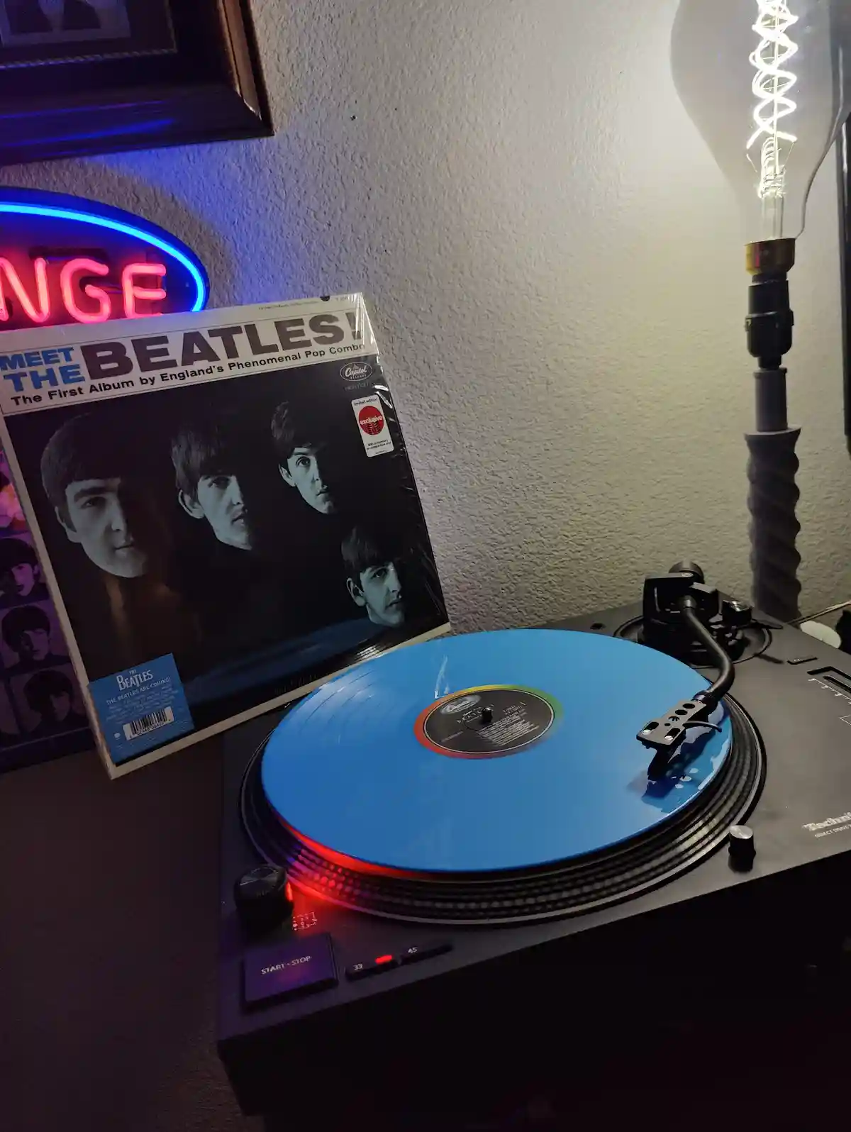 A vinyl record player with a bright blue record spinning, next to the album cover for 'Meet The Beatles!' The cover features…