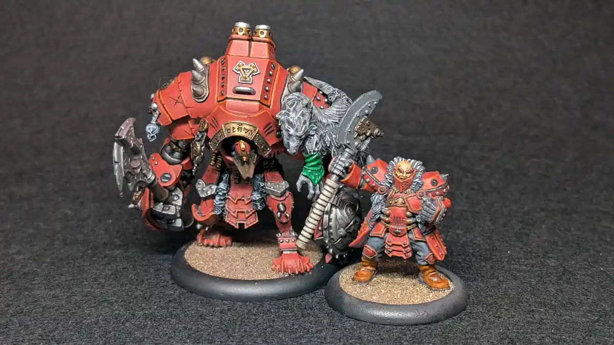 Two painted fantasy miniatures, one large red armored creature with a wolf-like head and one smaller red armored warrior…