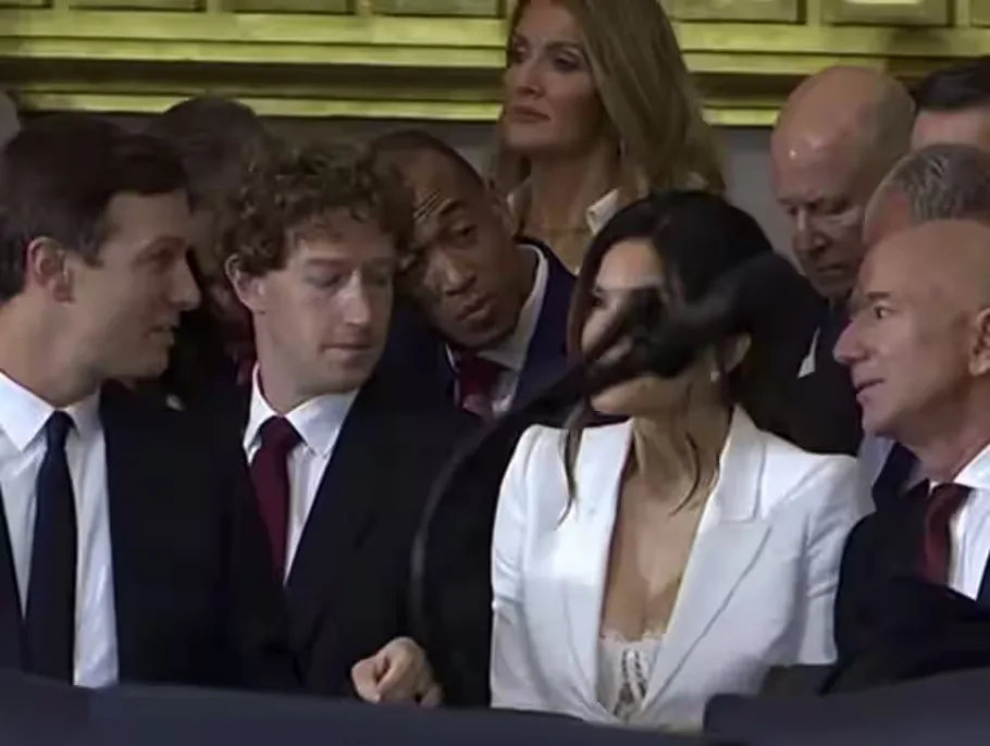 A group of formally dressed people, including a woman in a white blazer and a bald man in a suit, are gathered around a…