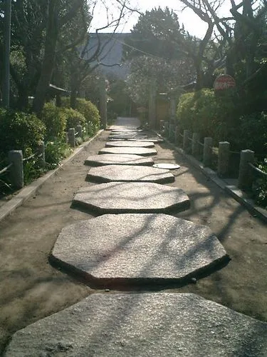 a photo of a path made of large, flat, octagonal stepping stones set in dirt, flanked by low stone railings and greenery…