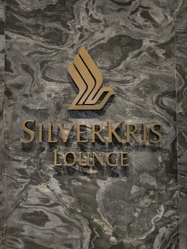 A close-up of a luxury sign for the SilverKris Lounge, featuring a gold logo and lettering mounted on a dark, veined marble…