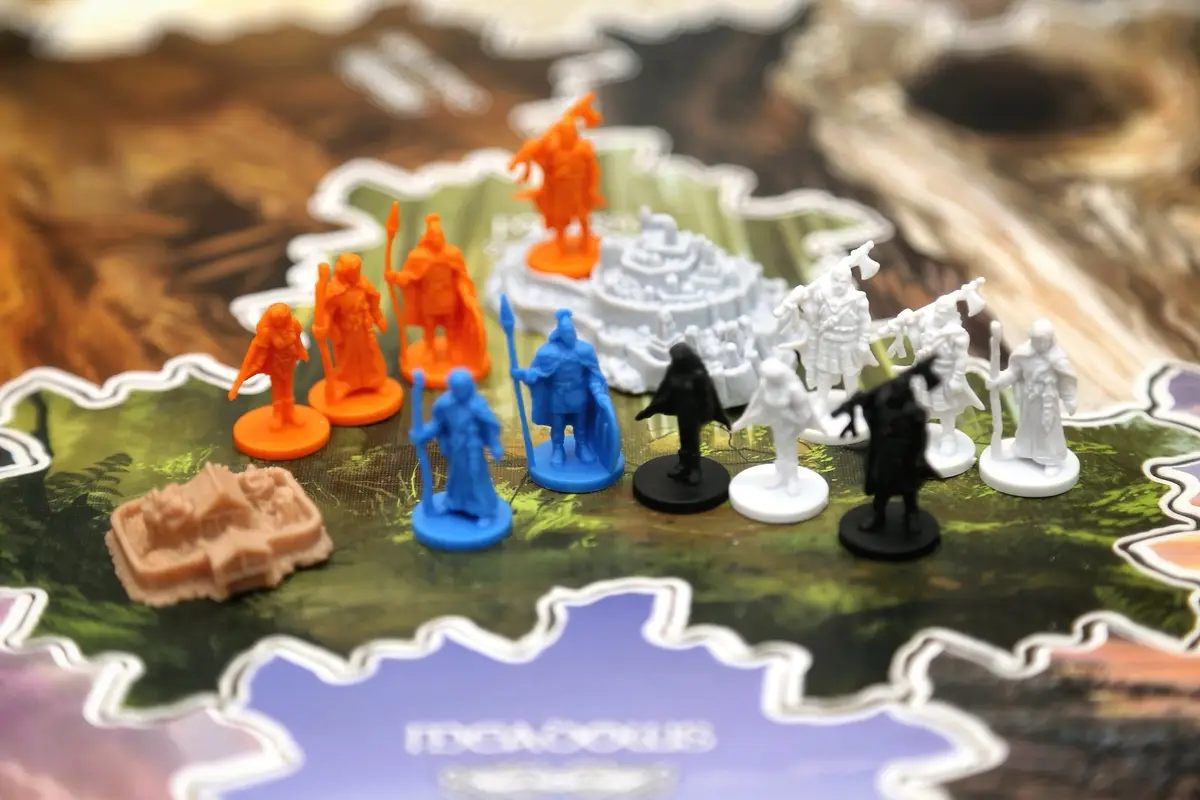A close-up photo of colorful fantasy miniatures on a game board, with orange figures prominently positioned near a castle…