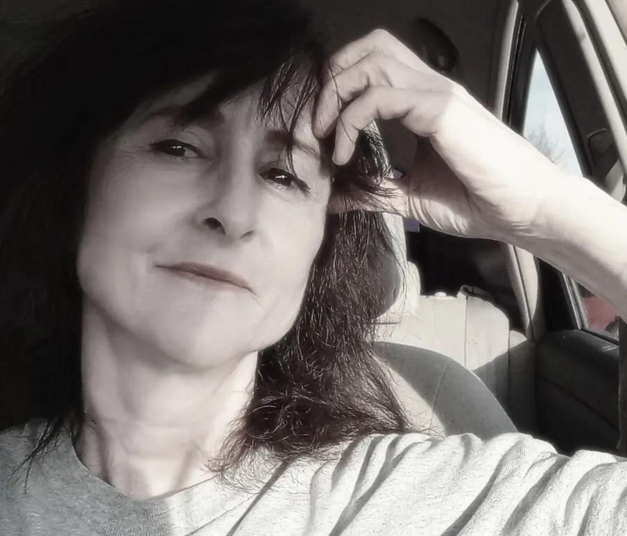 A black-and-white selfie of a woman sitting in a car, looking tired or exasperated while touching her hair. The overlaid…