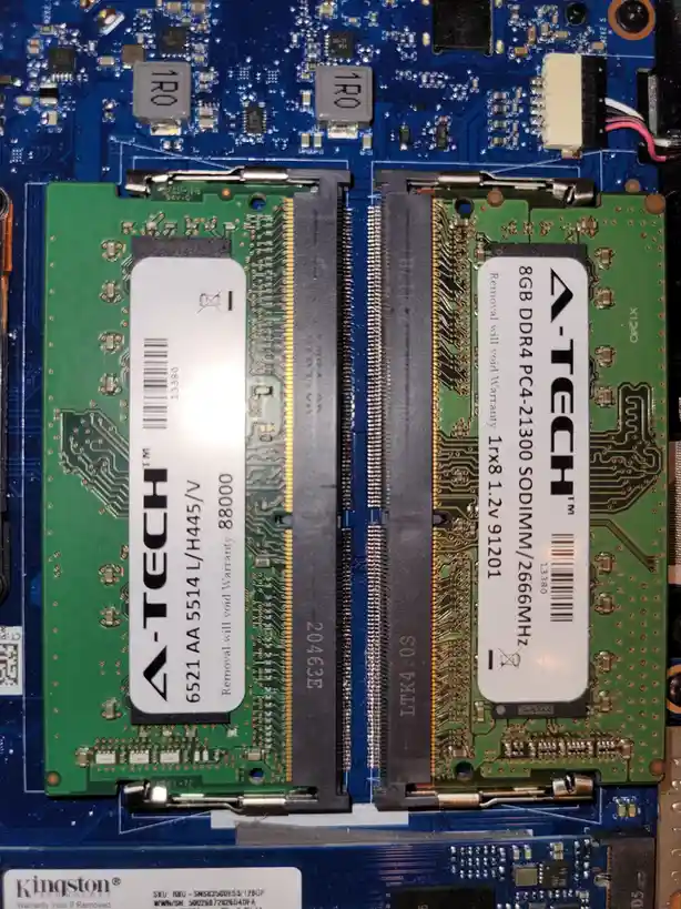 A close-up photo of two green A-Tech brand SODIMM RAM sticks installed in a laptop motherboard, with visible text on their…