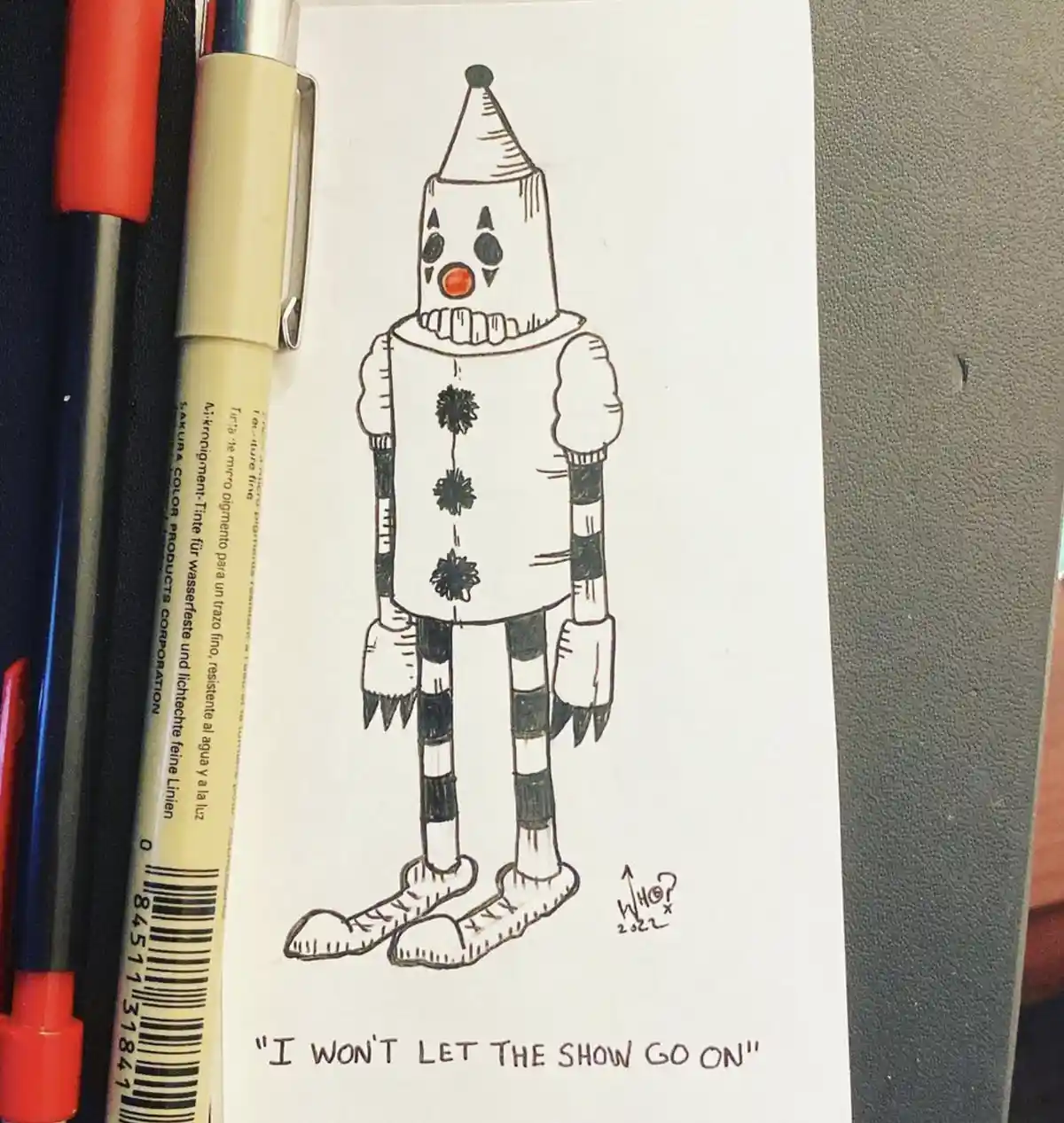 A hand-drawn sketch of a clown-like robot with a cone hat, black and white striped limbs, and a red nose, standing on a…