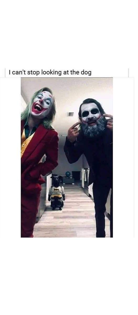 Two people dressed as the Joker from different movie versions stand in a hallway, both pointing at a small dog in the…