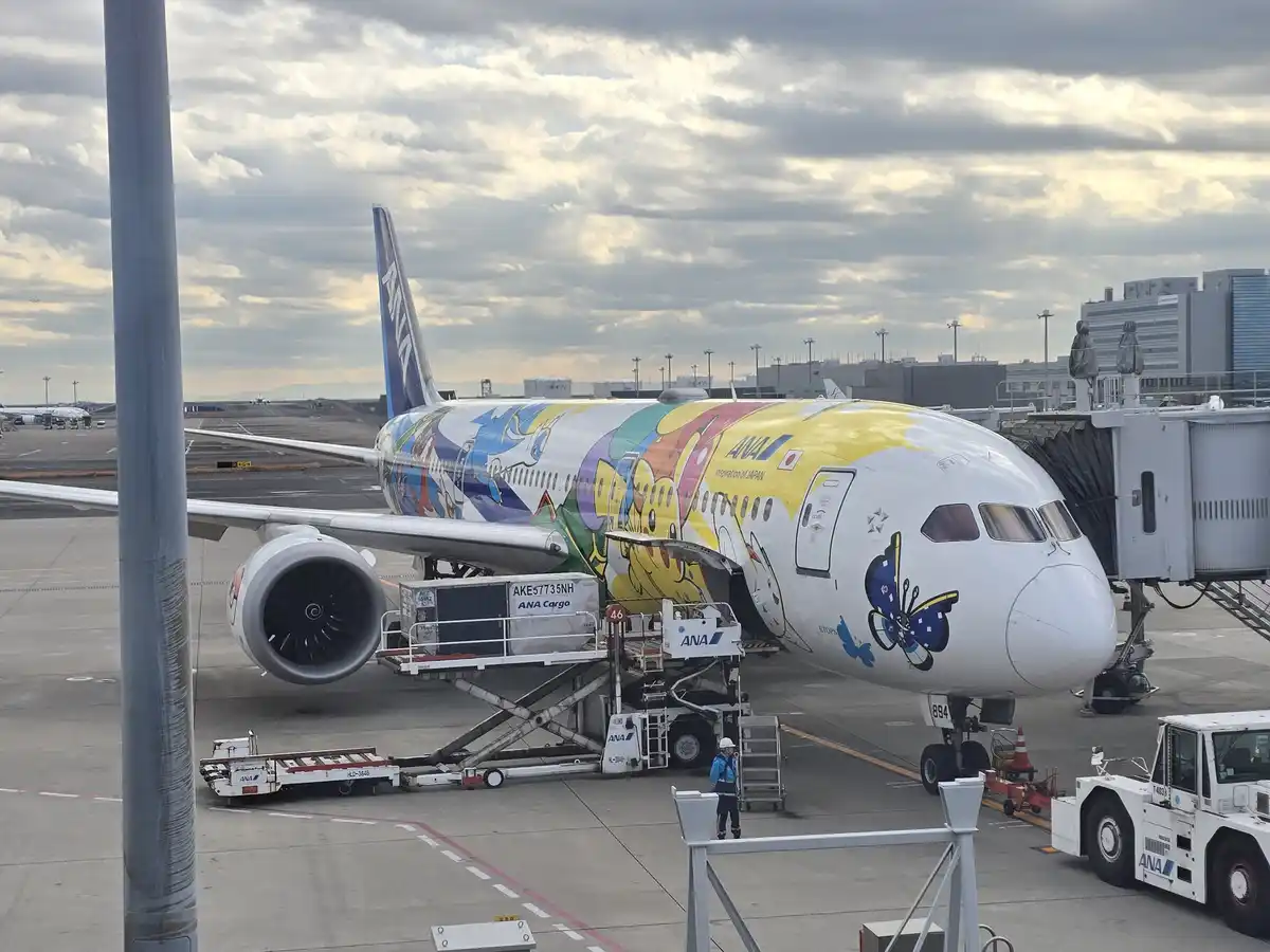 An ANA airplane with a colorful 'Inspiration of Japan' livery featuring cartoon characters is parked at an airport gate…