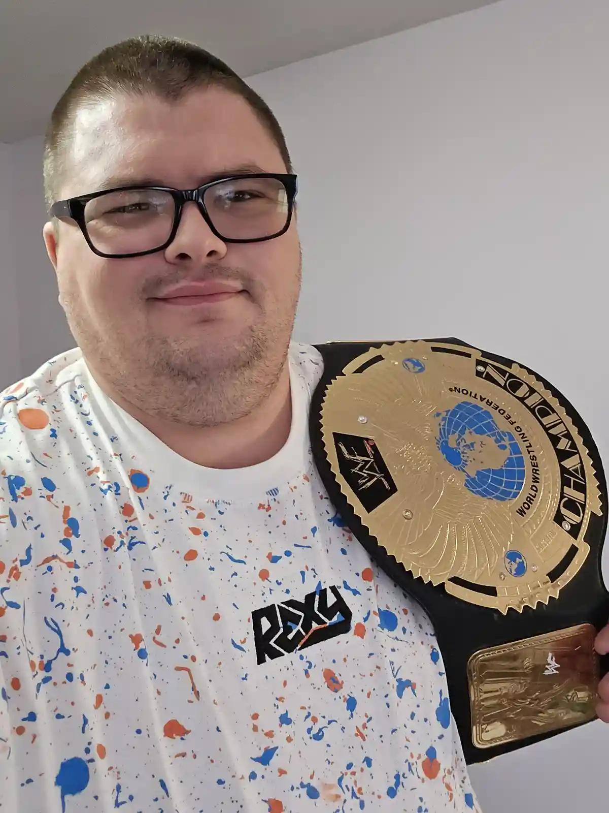 A man with short hair and black-rimmed glasses wears a white t-shirt with blue and orange splatters and the 'ROXY' logo…