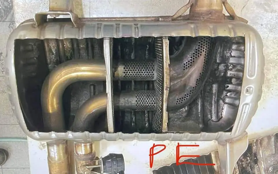 A close-up photo shows the internal components of a car's exhaust system, including pipes, baffles, and a perforated metal…