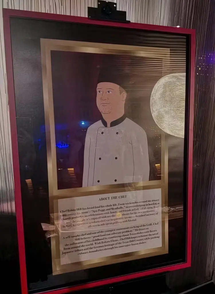 A framed portrait of a chef in a white uniform and black hat is displayed in a red frame with a glass cover. Below the…