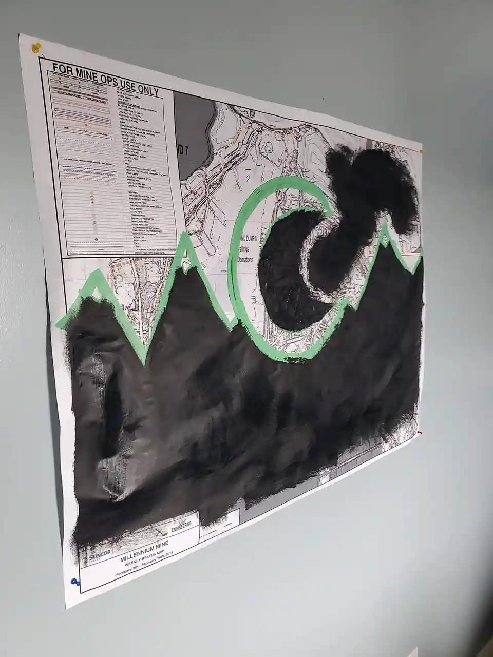 A mine operations map is pinned to a wall, with large sections covered in black marker and outlined in green. The letters…