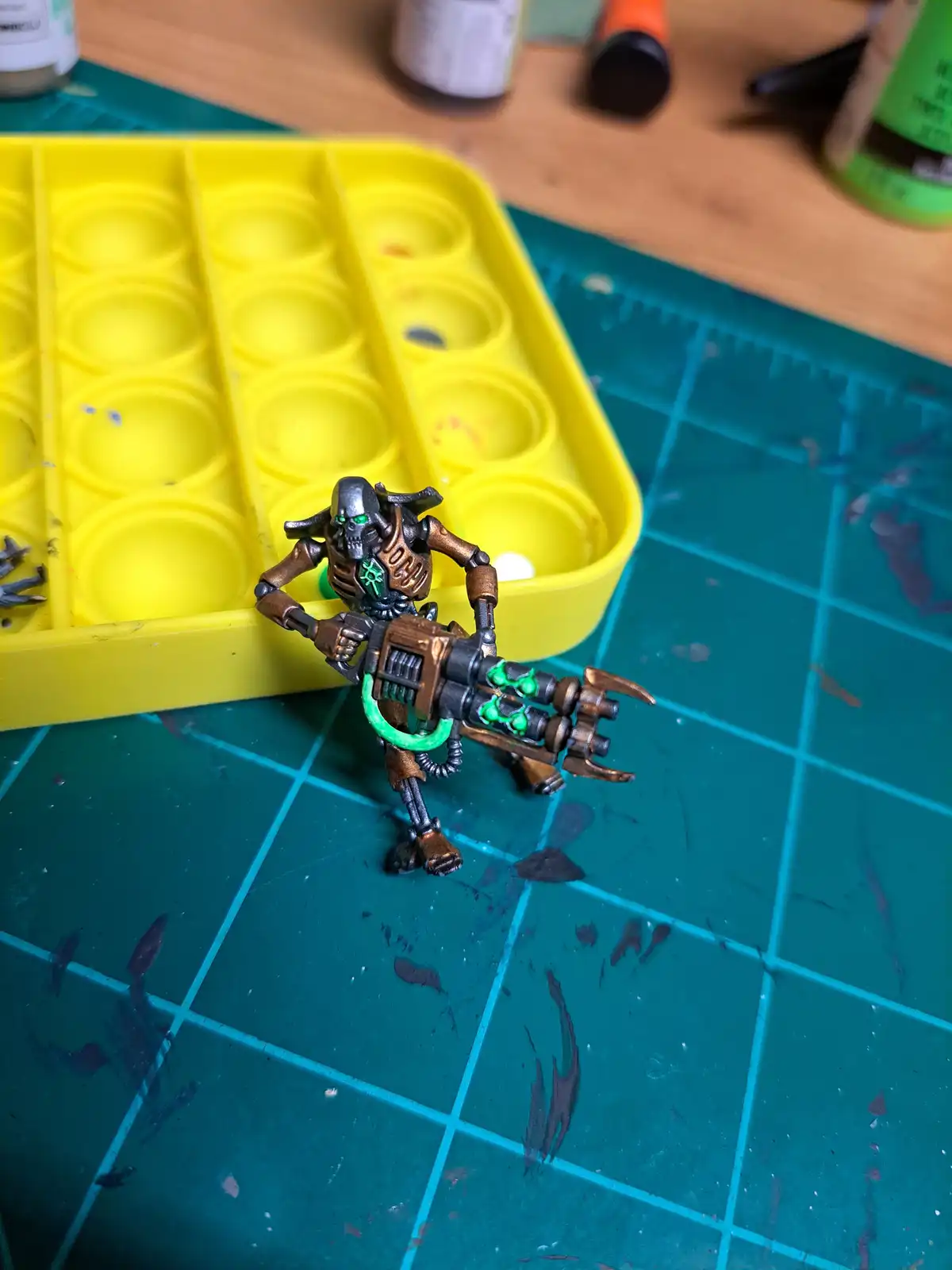 A painted miniature of a grim reaper-like figure with glowing green eyes and a large weapon stands on a green gridded…