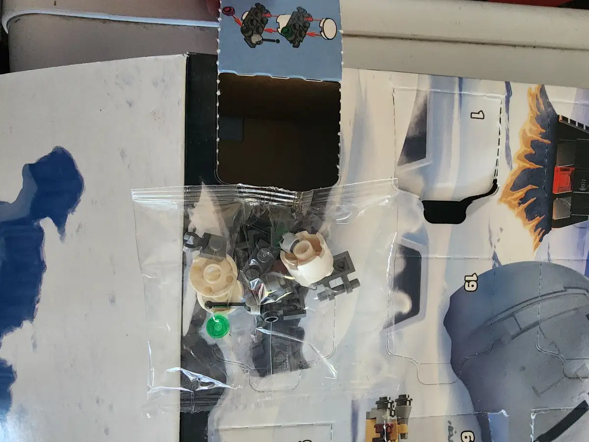 A close-up photo shows a partially opened LEGO set box with a clear plastic bag of assorted small LEGO pieces spilled out…