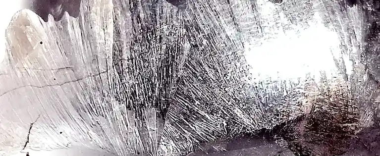 A close-up grayscale image shows a textured surface with intricate, layered patterns resembling frost, ice crystals, or…