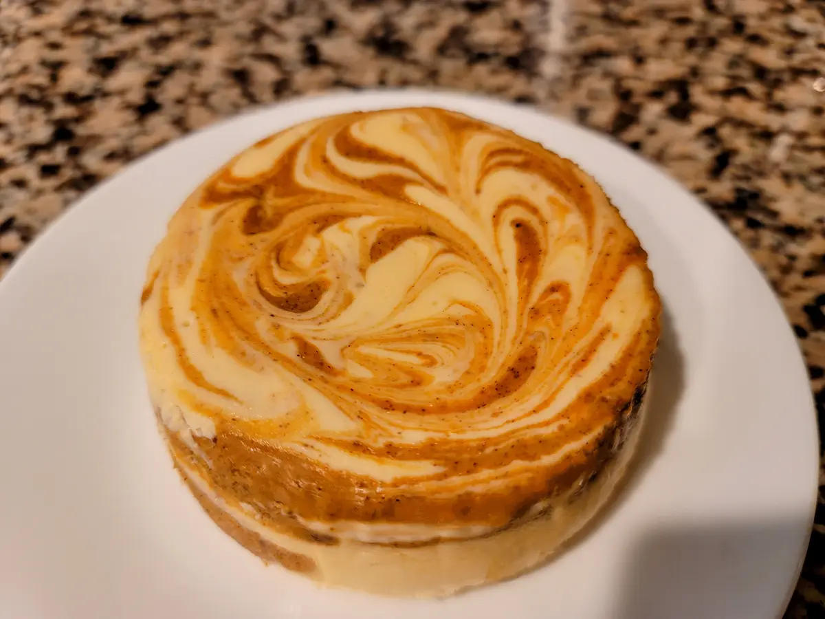 A round dessert with swirls of light and dark cream on a white plate, sitting on a speckled countertop, with text overlaid…