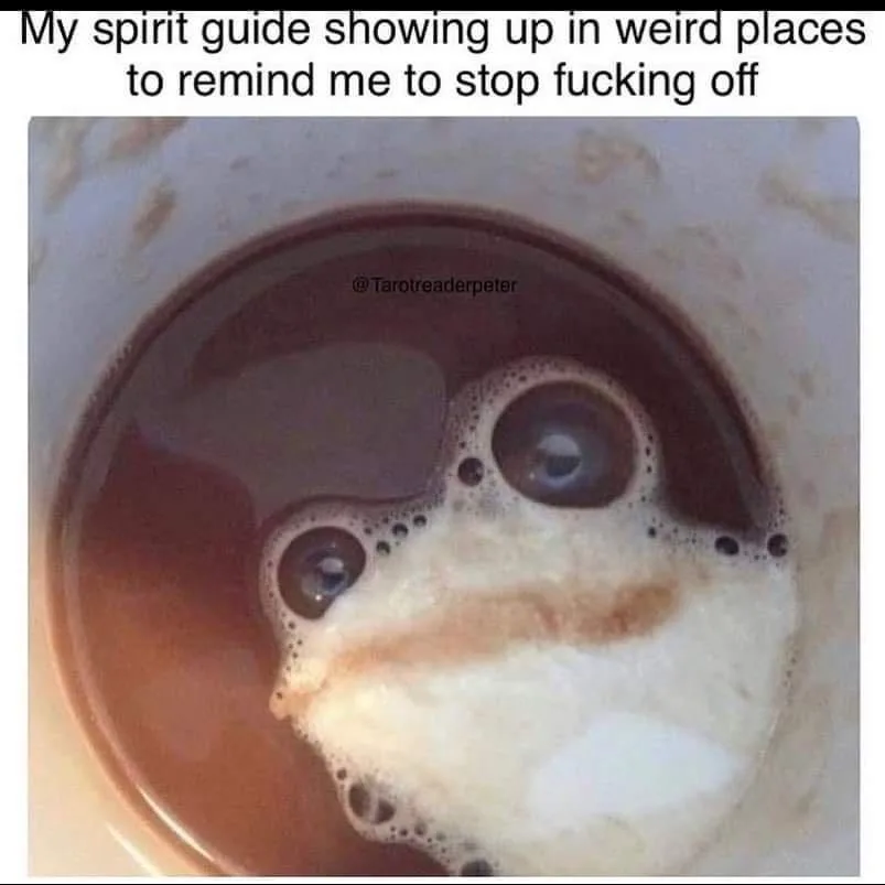 A close-up photo of coffee in a white mug, where the foam and liquid create a face-like pattern resembling a surprised or…
