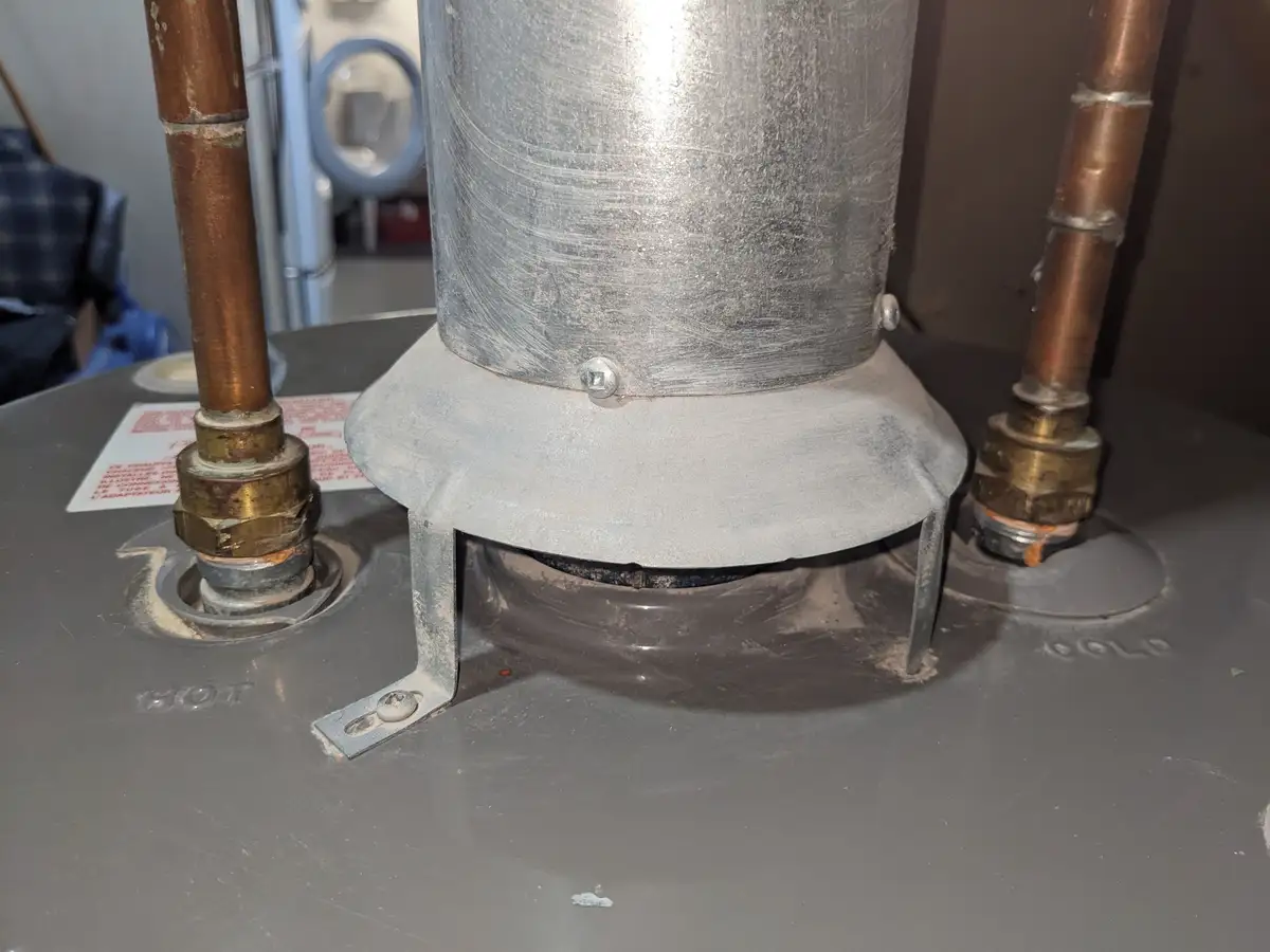 A close-up photo of a water heater's top, showing copper pipes connected to brass fittings, with the word 'HOT' stamped on…