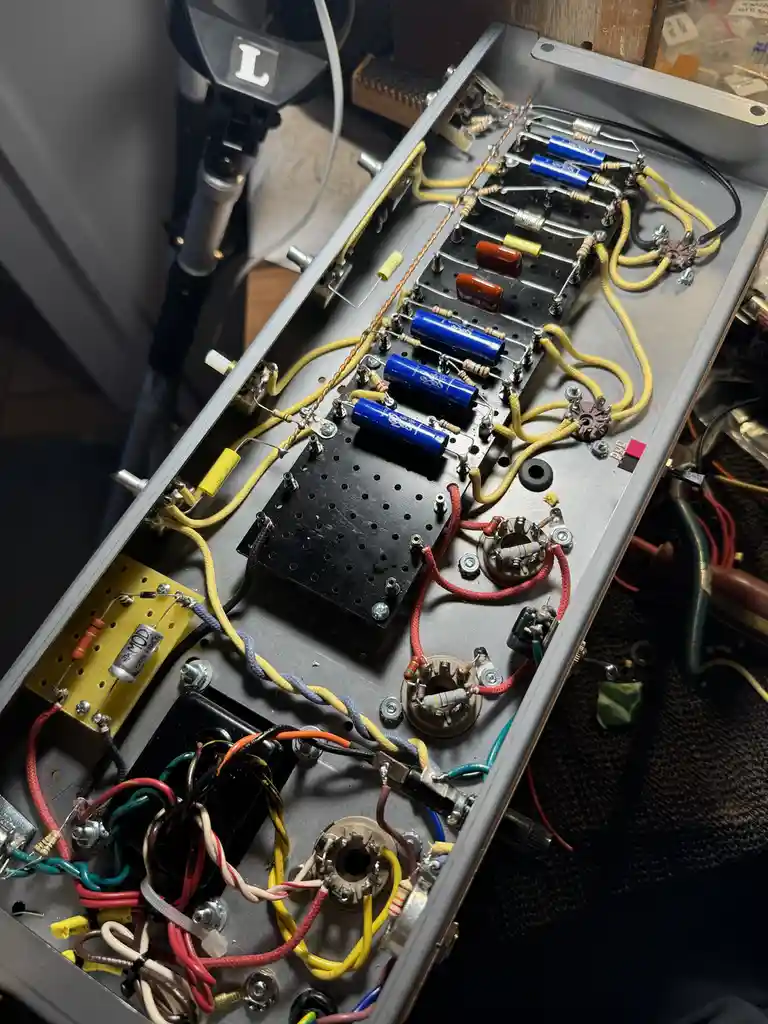 An overhead view of the open chassis of a tube amplifier, revealing a dense and chaotic tangle of colorful wires, resistors…