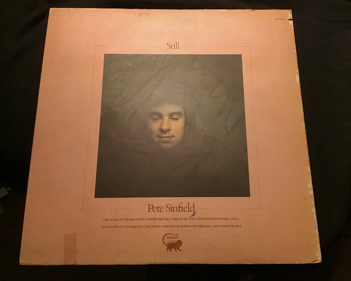 A close-up photo of a vintage, slightly worn peach-colored vinyl record album cover for Pete Sinfield's 1970 album 'Still'…