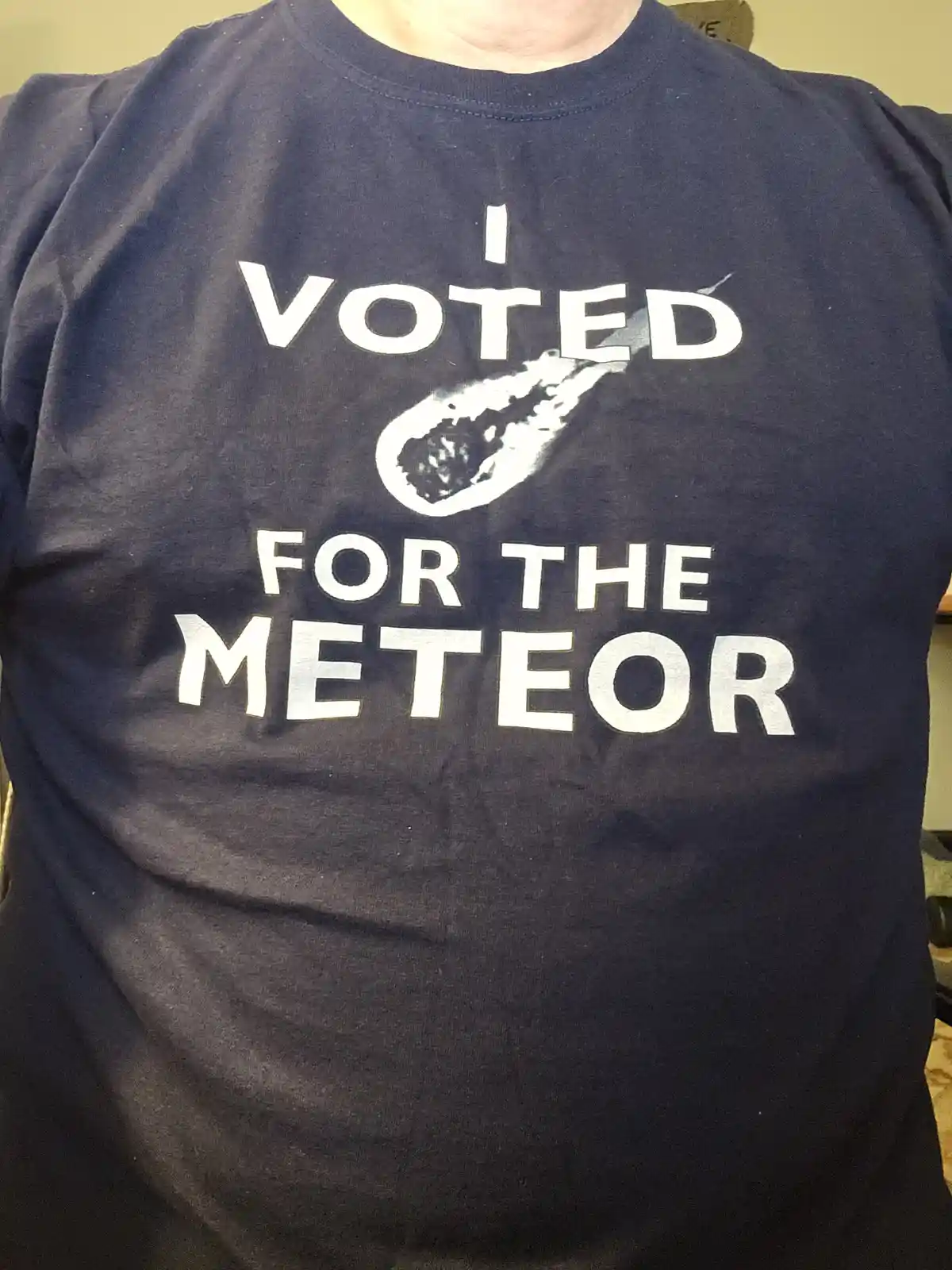 A person wears a dark blue t-shirt with white text that reads 'I VOTED FOR THE METEOR', with a graphic of a meteor streaking…