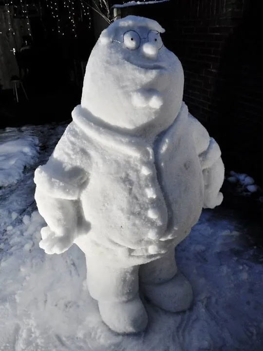 A snow sculpture of the cartoon character Peter Griffin, recognizable by his round head, glasses, and bulky body, stands in…
