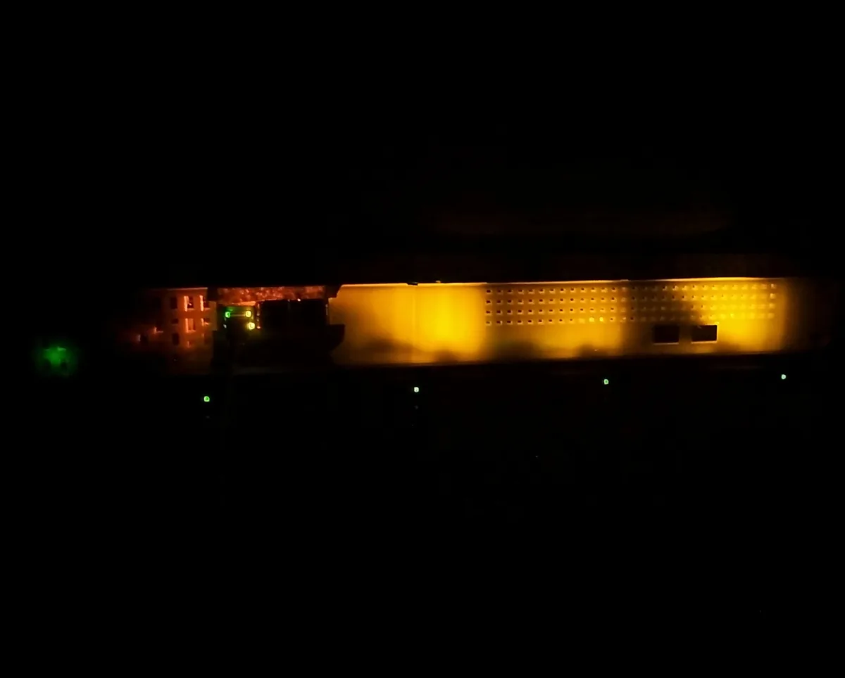 A dark photo shows a long, illuminated electronic device, possibly a server rack or network equipment, glowing with orange…