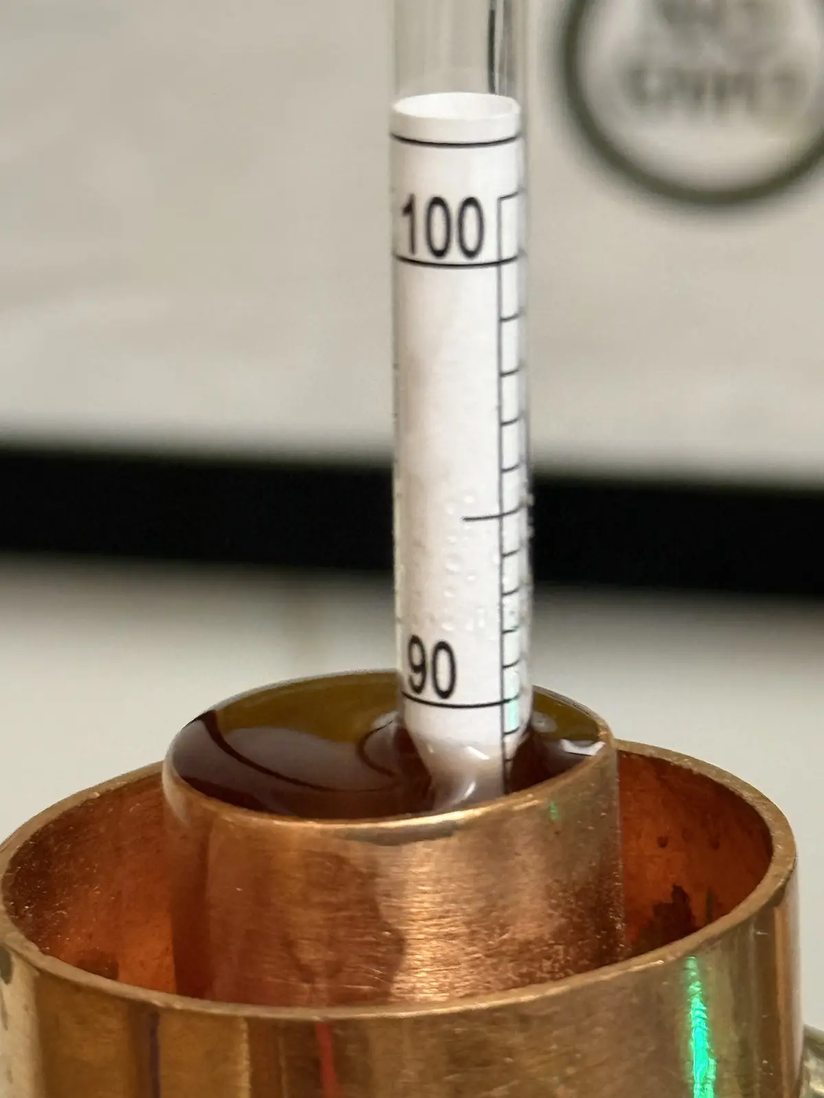 A close-up photo shows a glass graduated cylinder with measurement markings, including '100' and '90', partially submerged…