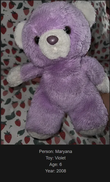 A purple plush teddy bear with white paws and snout sits on a strawberry-patterned fabric. Text overlaid at the bottom…